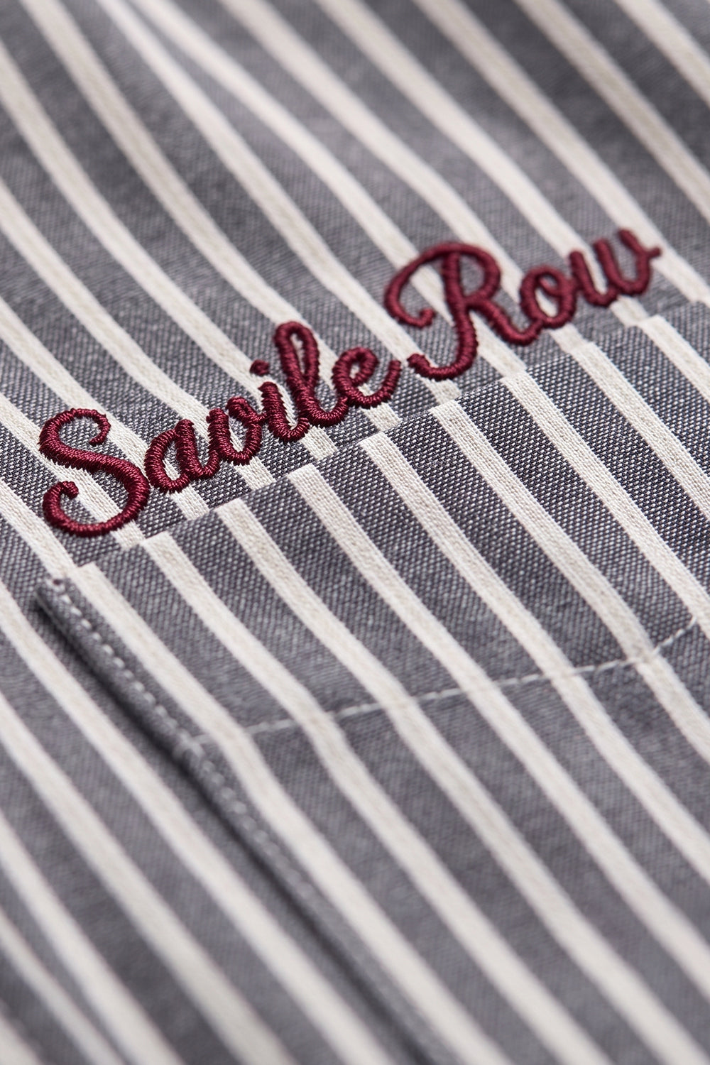 Macro close-up highlighting the premium red "Savile Row" script embroidery on the chest pocket of the Striped Shirt.
