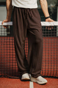 Man wearing dark brown tapered fit Pants with drawstring waist on a tennis court
